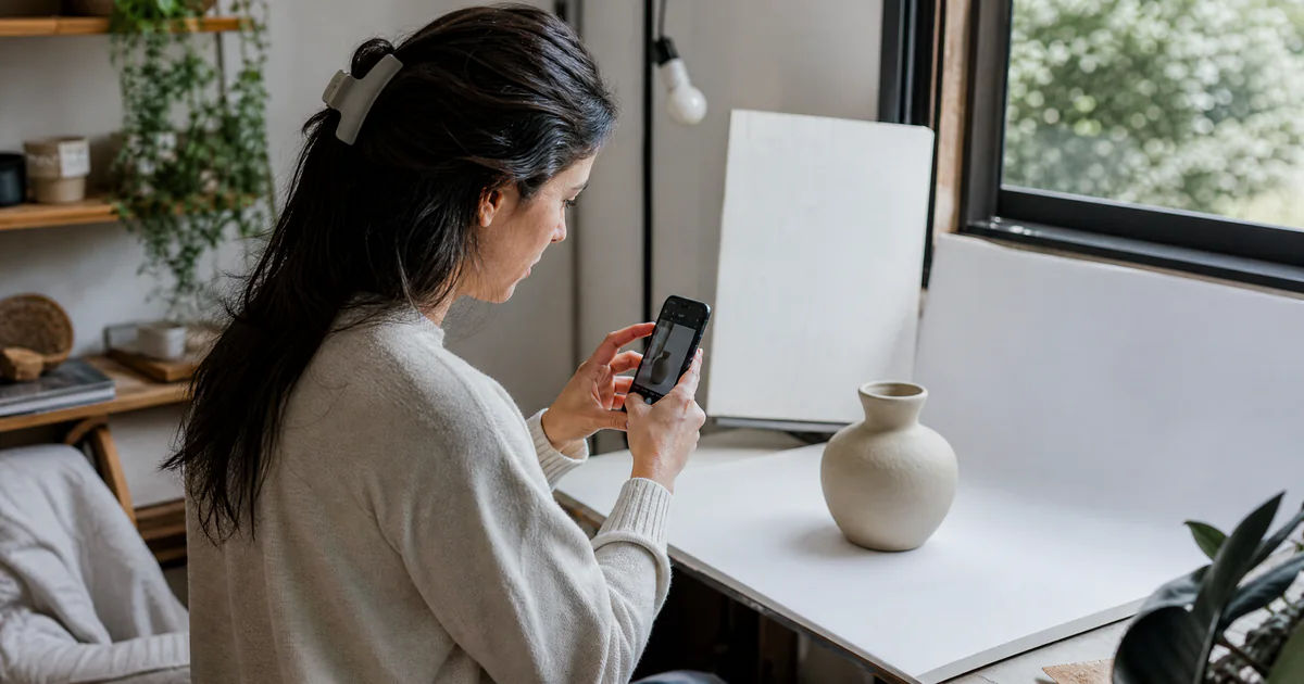 Empreendedora fotografando produtos com o celular num pequeno estúdio caseiro